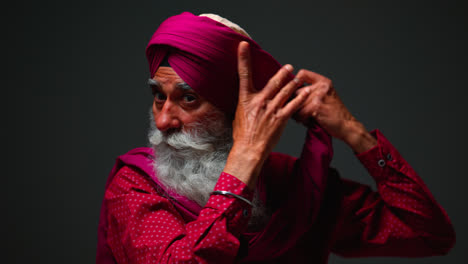 Fotografía-De-Estudio-Con-Iluminación-Tenue-De-Un-Hombre-Sikh-Mayor-Con-Barba-Atando-Una-Tela-Para-Un-Turbante-Contra-Un-Fondo-Oscuro,-Filmada-En-Tiempo-Real-1